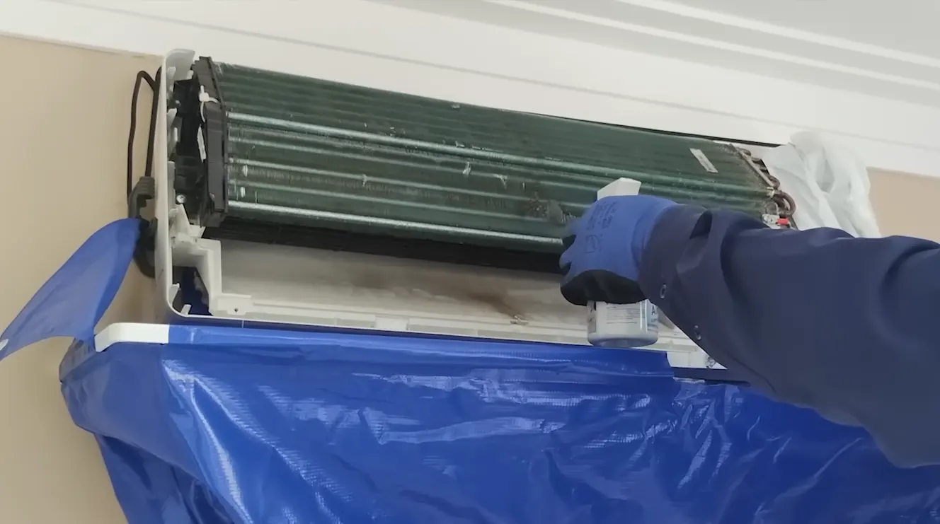Técnico lavando unidade externa de ar condicionado durante higienização